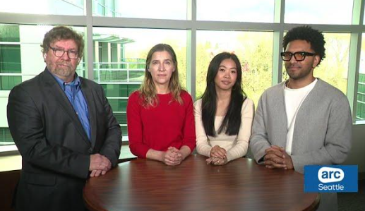 Four people standing around a table during an interview.