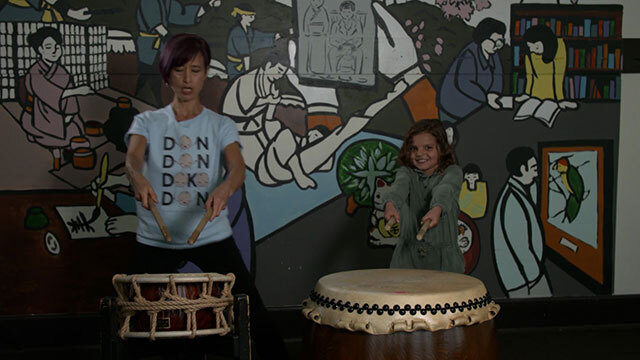 Woman and child stand next to each other, each behind a drum