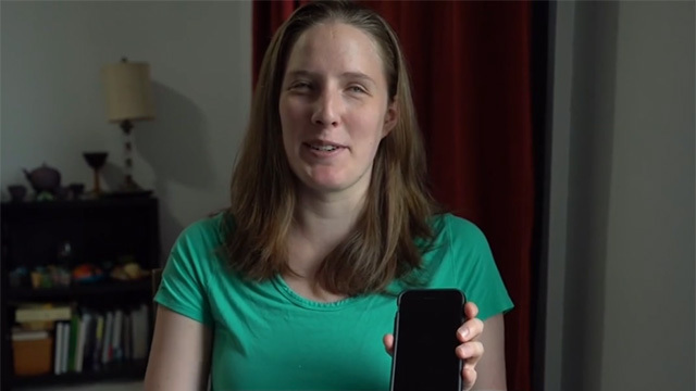 Woman with mid-length brown hair and green shirt holds up phone with black screen
