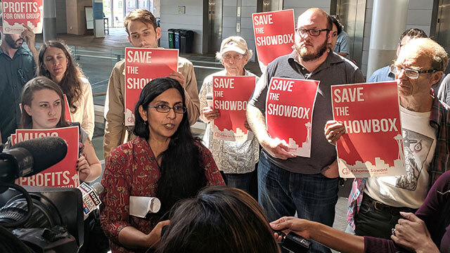 Former Councilmember Sawant stands surrounded by people with signs reading "Save the Showbox"
