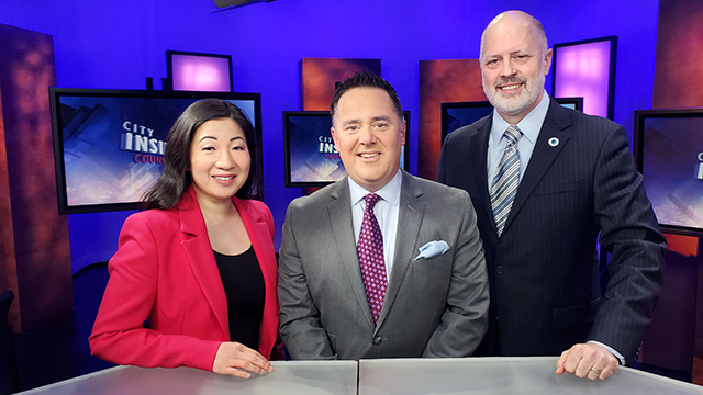 From left to right, Councilmember Woo, Brian Callanan, Councilmember Kettle stand behind desk in television studio