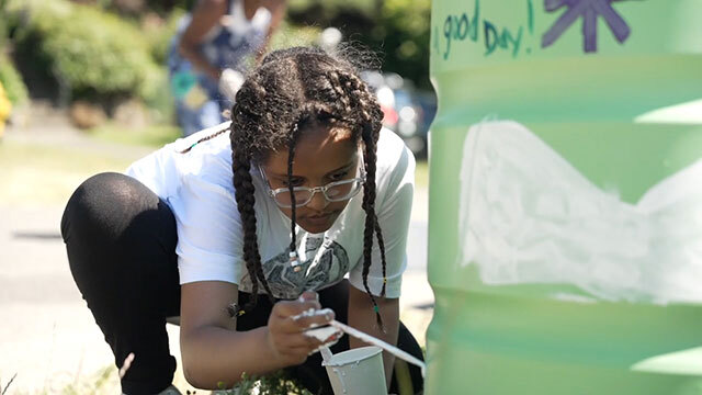 Black girl leans down, painting planter