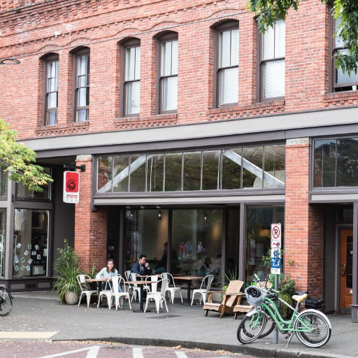The exterior of a brick building with people eating at tables on the sidewalk in front.