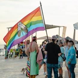 group of people standing on the pier while holding a pride flag