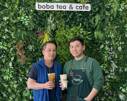 hyson boba co-owners stand in front of store sign with boba teas