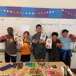 Photo of 5 kids standing in front of a white board holding prizes, participating in a Atlantic Street Center youth program.