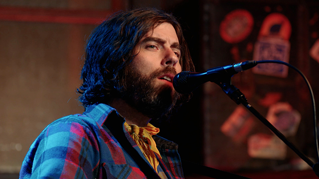 Bearded man in flannel sings into microphone