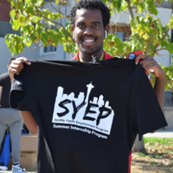 Man holding up a shirt from the Seattle Youth Employment Program that says "SYEP" over the Seattle skyline.