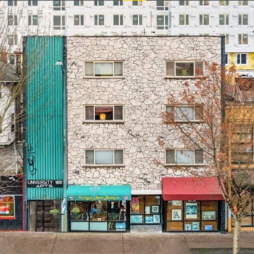 Apartment building with six windows, turquois siding on the left side, and white stone on the face of most of the building.