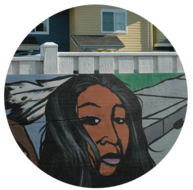 A mural with a painting of a Native woman on a wall in front of a row of houses