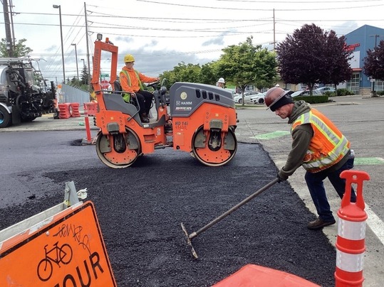 Workers in high-visibility gear work in the roadway to repave North 45th Street in Ballard.