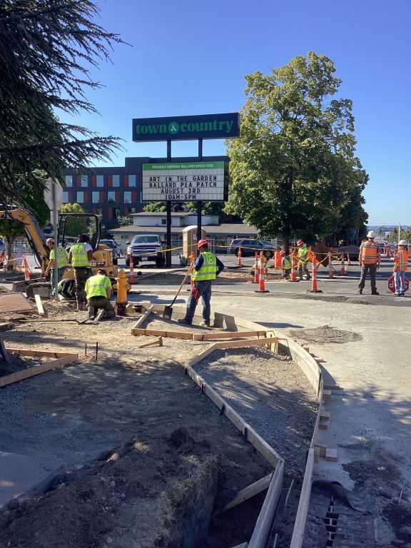 A photo of construction crews installing new sidewalks and roadway on the southeast corner of 15th Ave NW and NW 57th St.