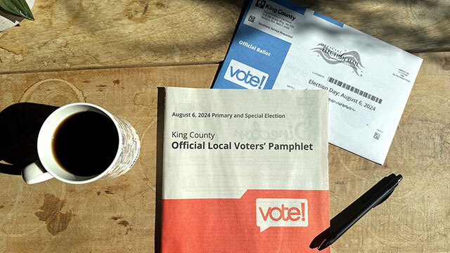 Photo of coffee mug, King County voters' pamphlet, pen, and ballot envelope from above