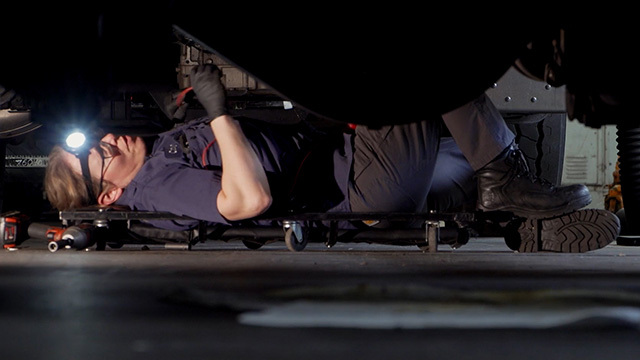 Mechanic with headlamp lays on dolly, working under vehicle