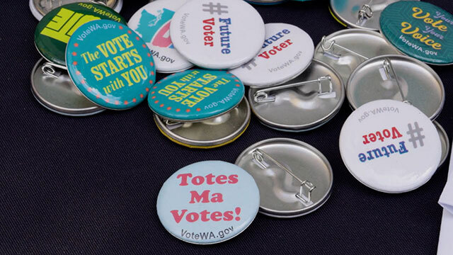 Pile of various multicolored buttons with phrases about voting, one reads "The VOTE STARTS with YOU"