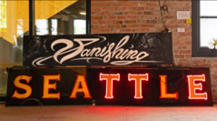 Two neon signs leaning against a brick wall that read "Vanishing Seattle."