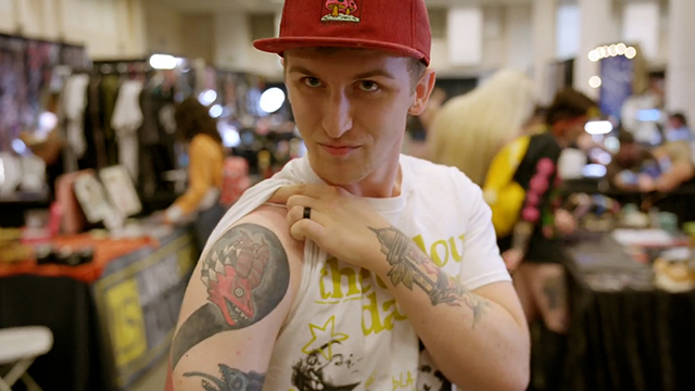 Person in red baseball cap pulls white t-shirt sleeve up to show red and black dragon tattoo