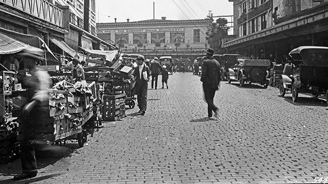 Black and white image of people walking around Pike Place Market, early 1900s