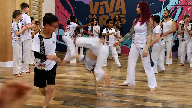 Kids and instructors dressed in white stand around a studio, some perform acrobatic moves