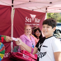 A boy receives a prize from a Sea Mar employee at a neighborhood festival information booth