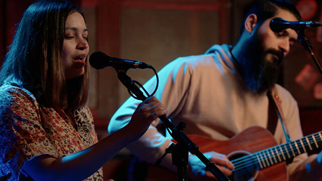 Two people perform onstage, one sings, one plays guitar