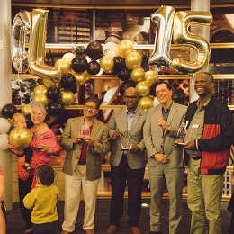 A group of people, smiling, standing under an arch of balloons at a celebration