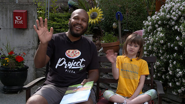 Man and kid sit on bench outdoors, both wave at camera