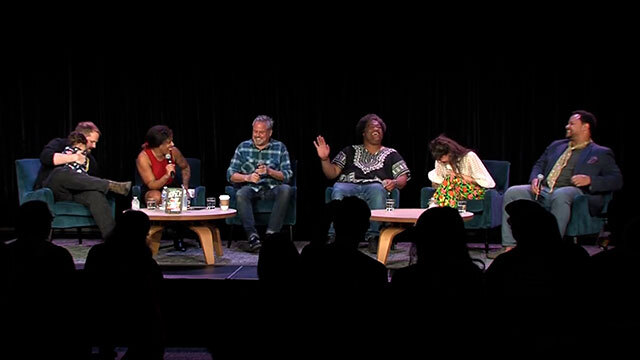 Six people, one holding baby, laugh onstage