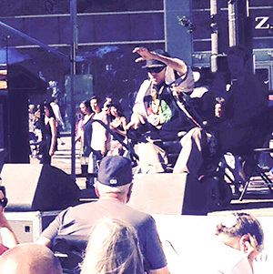 An older photo of a performer in a wheel chair raising their hand toward the audience