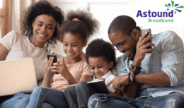  A family of four sits together on a couch, engaged with various electronic devices. The Astound Broadband logo is visible