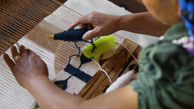 Top view of person's shoulder and hands as they weave in a loom