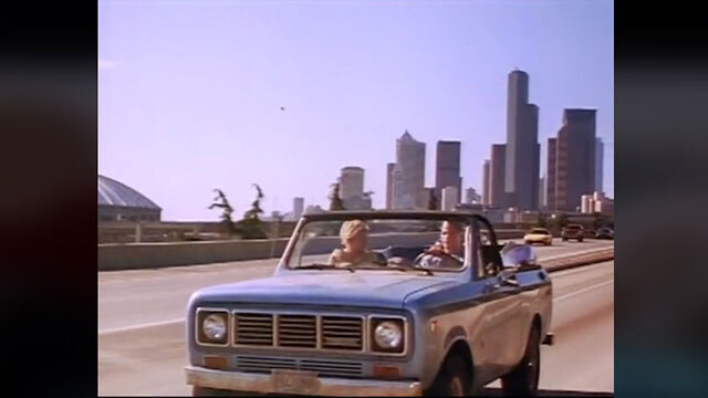 Seattle skyline with two people in blue convertible car on highway in foreground