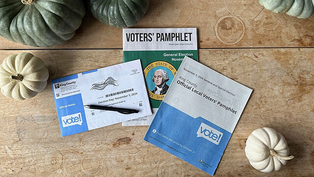 King County ballot and voters' pamphlet and City of Seattle voters' pamphlet on wooden surface with white and green pumpkins