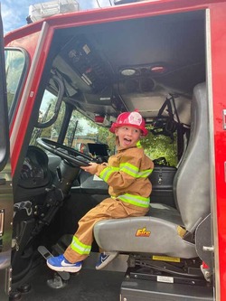 Child in a firefighter costume sits in the driver's seat of Seattle Fire Engine 26