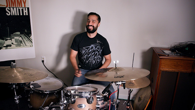 Ehssan Karimi smiles from behind drum kit