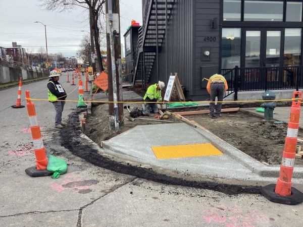 Three people in hard hats and brightly colored jackets set out long pieces of wood to create guides for soon-to-be poured concrete. 