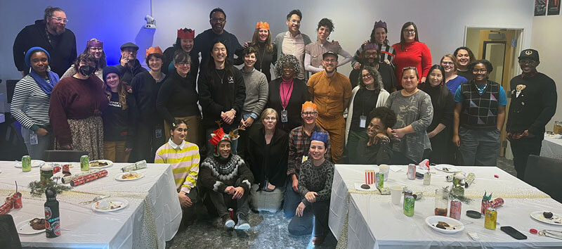 A group of multi-racial people pose in a holiday decorated room with tables full of food and drink