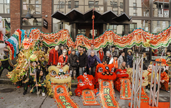 Lion dancers stand with props and a group of people in front of brick building