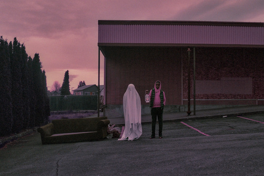 photo of a ghost and a man holding a lantern standing together in a parking lot