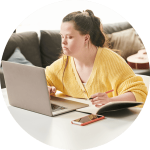Young woman with a disability writing in a notebook and working on an open laptop