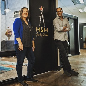 A woman and man of color standing in front of a black door with sign saying M&M jewelry studio