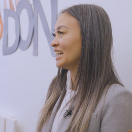 A woman standing at profile smiling, wearing a gray suit jacket.