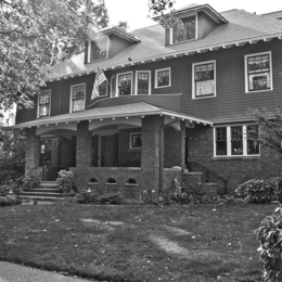 A black and white photo of a two story house with a brick front porch.