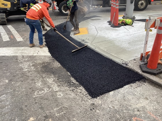 Crews paving asphalt around new ADA-compliant curb ramps at southeast corner of Rainier Ave S and S Massachusetts St.