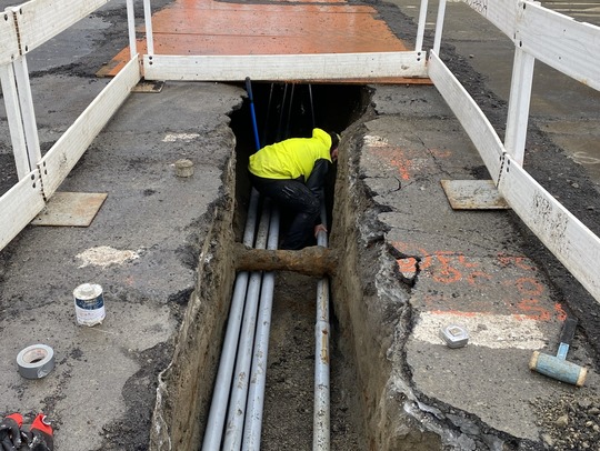 Crews installing electrical conduits beneath utility pipes. 