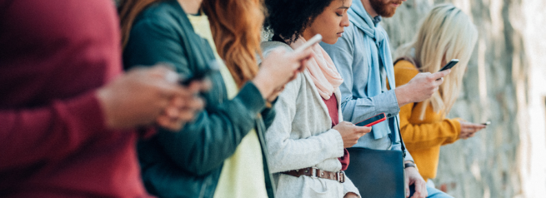 A header with a group of people leaning up against a wall looking at their smart phones.