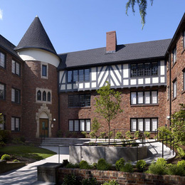 The courtyard of a brick, three-story apartment building with a white and blue design on the top level and center conical tower.