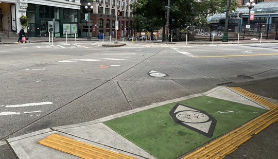 The green panel on the bike lane that rosses the intersection is wider, with two directional arrows to help cyclists know their position.