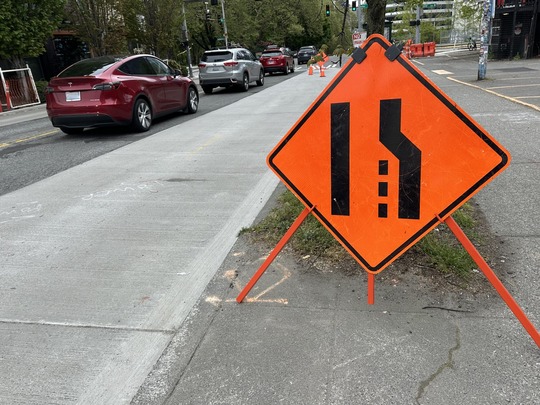 Image of 'right lane closed ahead' traffic sign and vehicles driving on Denny Way