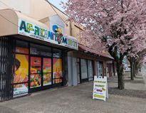 A storefront with colorful awning that reads "Africanita Market" with a blooming cherry tree along sidewalk in front